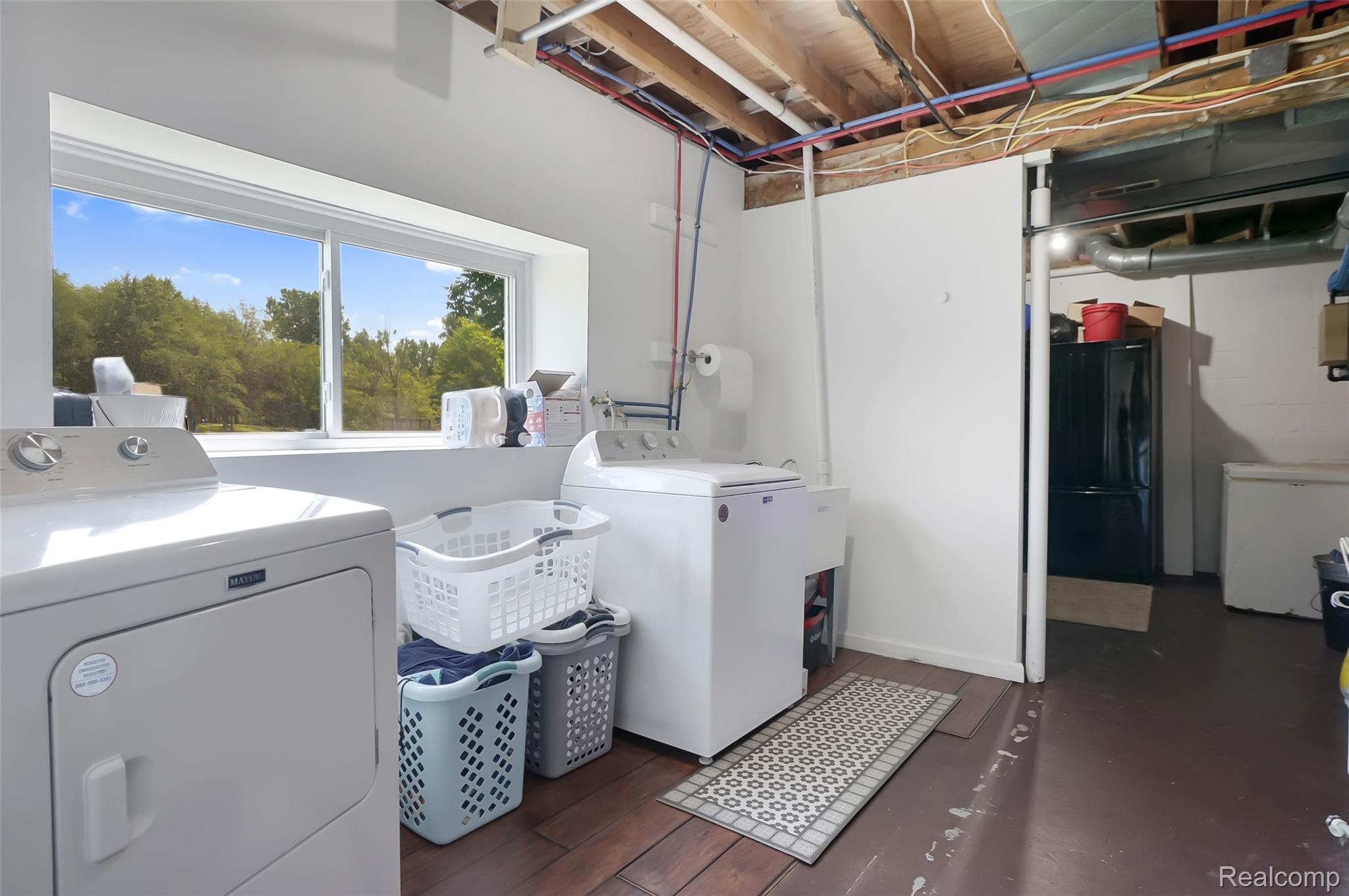 6050 Brophy Road Howell, MI 48855 - Photo 21 of 27 Laundry area featuring a large window, exposed ceiling joists with visible piping, a utility sink, and wood-finish flooring