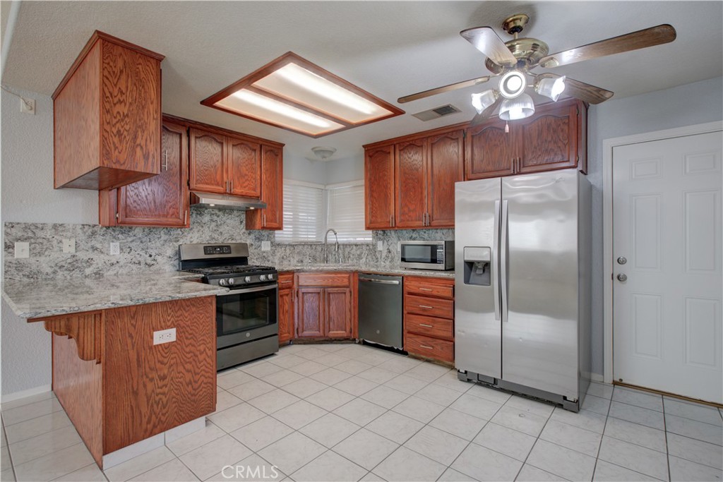 2341 Mesquite Court Merced, CA 95348 - Photo 3 of 17 a kitchen with stainless steel appliances granite countertop a refrigerator a sink dishwasher a stove with wooden cabinets and floor