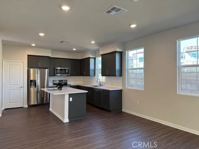 a large kitchen with stainless steel appliances granite countertop a stove top oven a sink dishwasher and a refrigerator with wooden floor