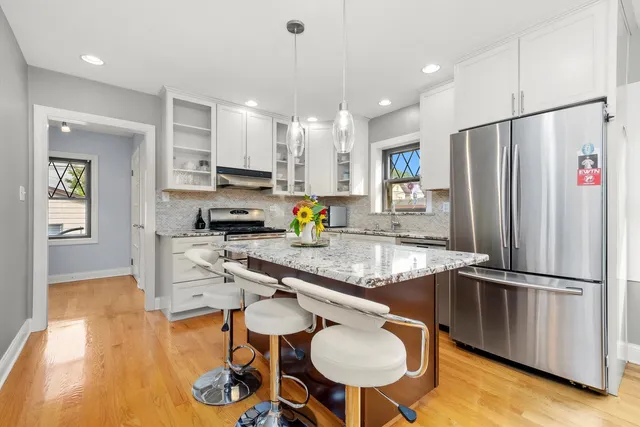 a kitchen with stainless steel appliances granite countertop a refrigerator a sink dishwasher a stove and a dining table with wooden floor