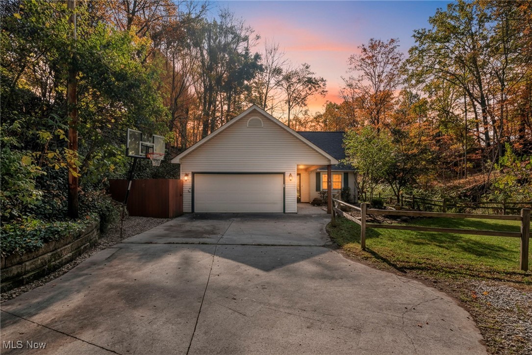 View of front of house with driveway, a garage, and view of wooded area