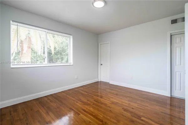 a view of an empty room with wooden floor and a window