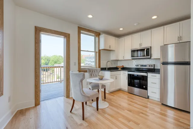 a kitchen with a refrigerator a stove top oven a sink and a dining table with wooden floor