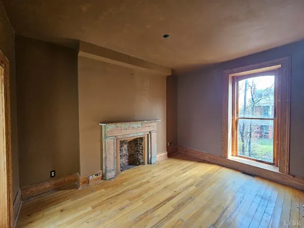 an empty room with wooden floor a fireplace and windows