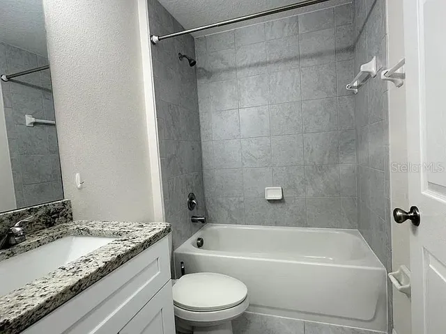 a bathroom with a granite countertop bathtub shower sink vanity and toilet