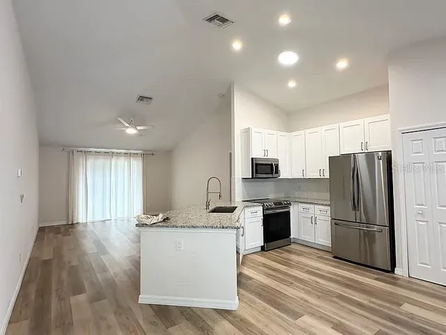 a kitchen with stainless steel appliances granite countertop a refrigerator a sink dishwasher a stove and white countertops with wooden floor