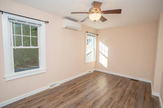 an empty room with wooden floor chandelier fan and windows
