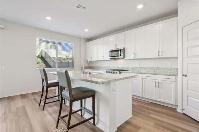 a kitchen with stainless steel appliances granite countertop a stove a refrigerator a microwave oven with white cabinets and wooden floor