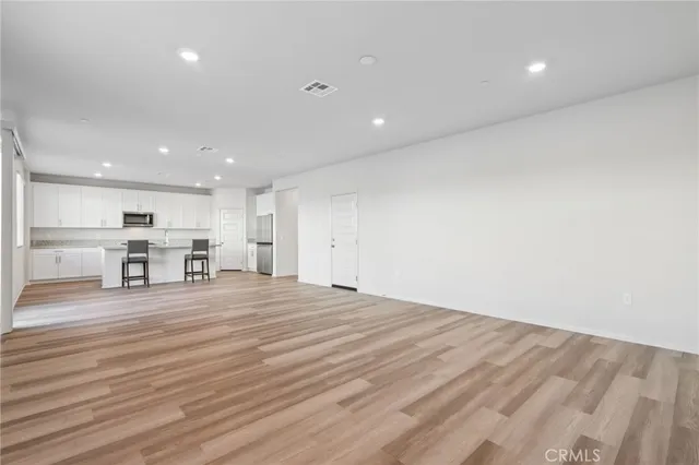 a big room with wooden floor and a kitchen view