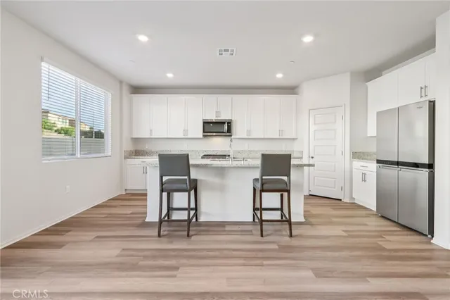 a kitchen with stainless steel appliances granite countertop a refrigerator a stove top oven and a dining table with wooden floor