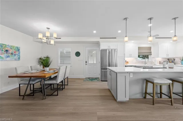 a dining hall with stainless steel appliances kitchen island granite countertop a table chairs sink refrigerator and microwave