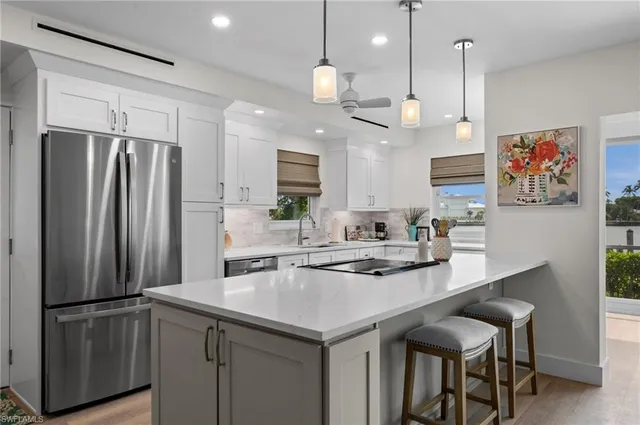 a kitchen with kitchen island stainless steel appliances a dining table chairs sink and white cabinets