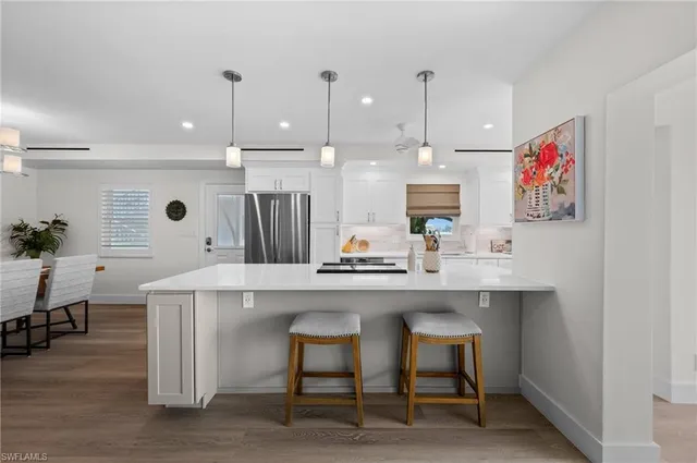 a kitchen with kitchen island stainless steel appliances a dining table chairs sink and white cabinets