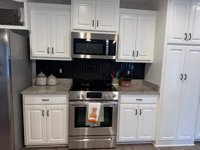 a kitchen with stainless steel appliances granite countertop white cabinets and a stove a refrigerator with white cabinets