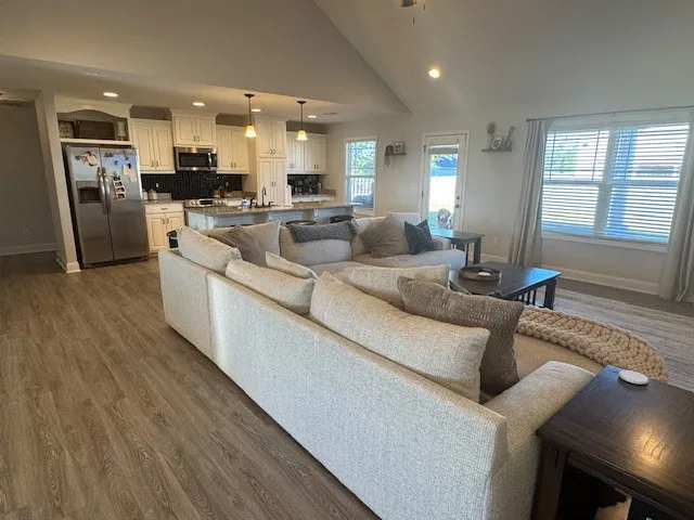 a large living room with stainless steel appliances kitchen island granite countertop a large kitchen island a stove a refrigerator a sink a dining table and chairs with wooden floor