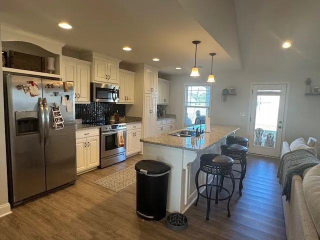 a kitchen with stainless steel appliances granite countertop a refrigerator a sink dishwasher a stove and white cabinets with wooden floor