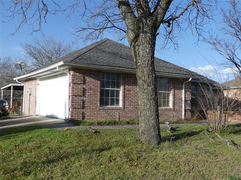 View of side of home featuring driveway, a yard, a shingled roof, a garage, and brick siding