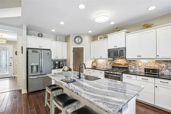 a kitchen with stainless steel appliances granite countertop a stove top oven a refrigerator a sink and white cabinets with wooden floor