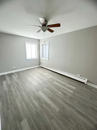 an empty room with wooden floor ceiling fan and windows