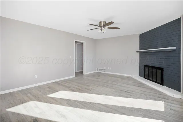 a view of a livingroom with a fireplace a ceiling fan and wooden floor
