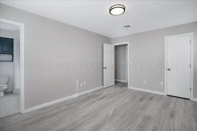 a view of an empty room with wooden floor and a bathroom