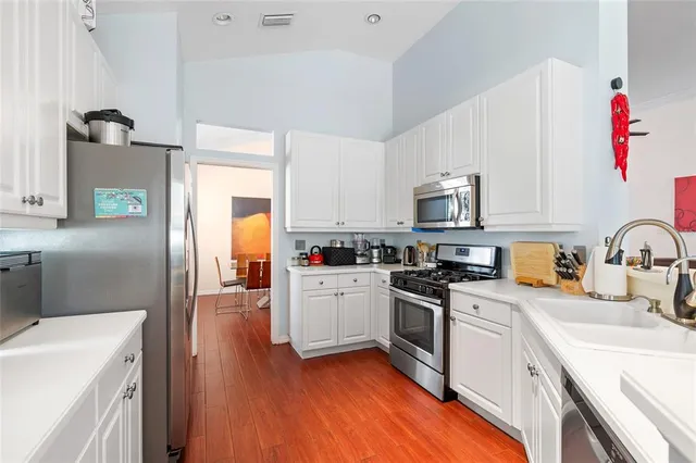 a kitchen with stainless steel appliances granite countertop a refrigerator a stove top oven a sink dishwasher and white cabinets with wooden floor