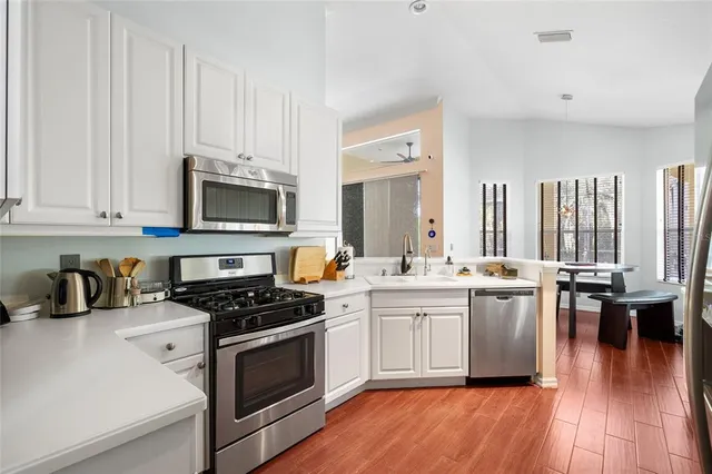 a kitchen with stainless steel appliances a white stove top oven a sink dishwasher and white cabinets with wooden floor
