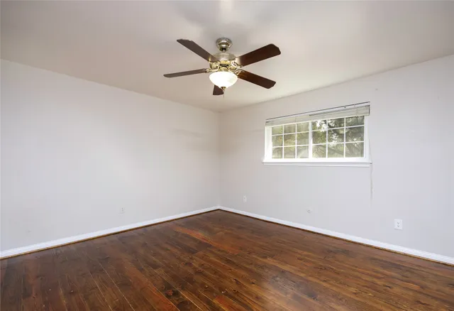 a view of an empty room with wooden floor and a ceiling fan