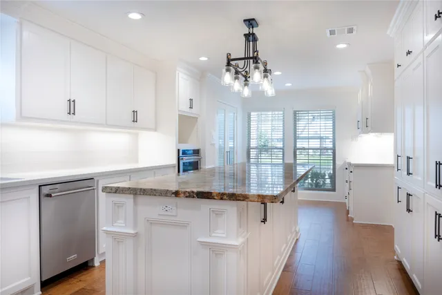 a kitchen with stainless steel appliances kitchen island granite countertop a stove a sink and white cabinets with wooden floor