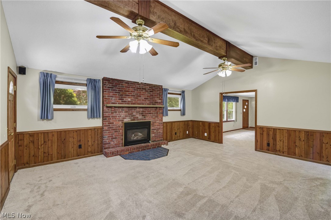 301 Crosse Road Amherst, OH 44001 - Photo 19 of 49 Spacious living area featuring a brick fireplace with a gas insert, vaulted ceiling with exposed wood beam, two ceiling fans, and wood paneling along the lower walls