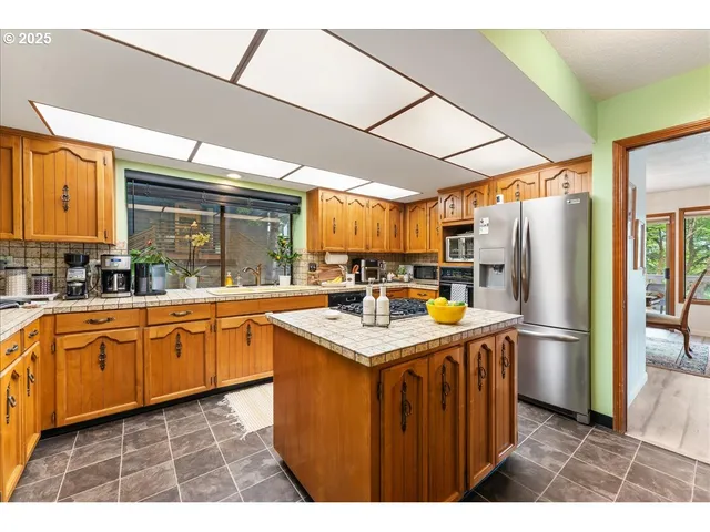 a kitchen with stainless steel appliances kitchen island granite countertop a sink refrigerator and cabinets