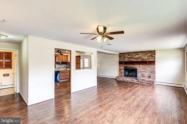 an empty room with wooden floor a ceiling fan and a kitchen