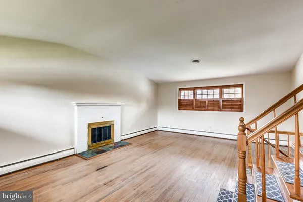 a view of an empty room with wooden floor fireplace and a window
