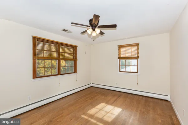 an empty room with wooden floor ceiling fan and windows