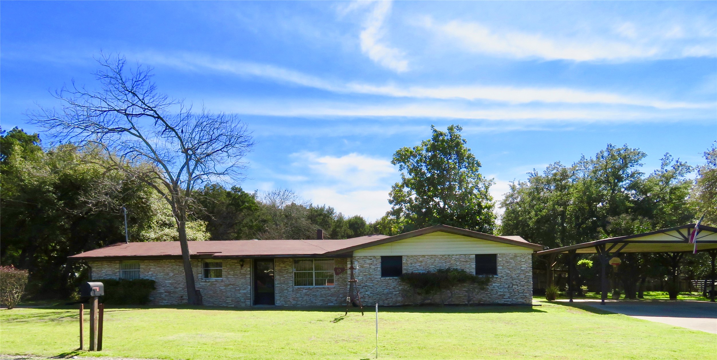 Single-story residence featuring a stone veneer facade, brown shingle roof, and a prominent carport
