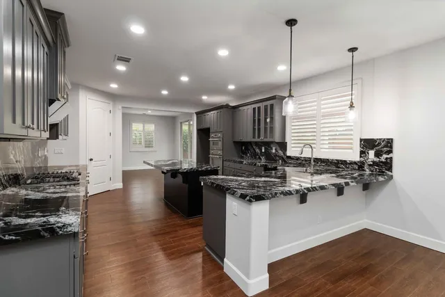 a kitchen with stainless steel appliances granite countertop a stove top oven a sink dishwasher a refrigerator and a cabinets with wooden floor