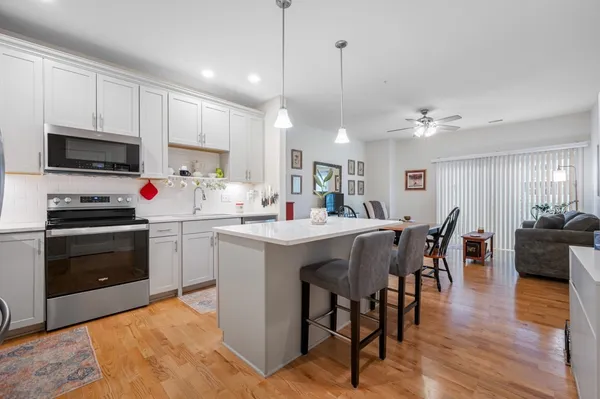 a kitchen with stainless steel appliances kitchen island granite countertop a stove a sink a microwave a dining table and chairs with wooden floor