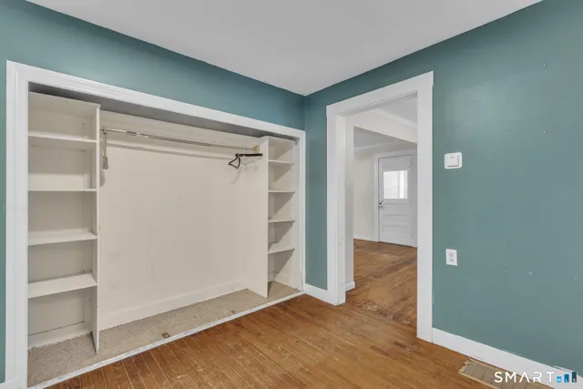 a view of an empty room with wooden floor and closet
