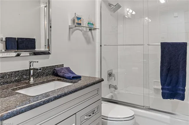 a bathroom with a granite countertop sink a toilet a mirror and shower