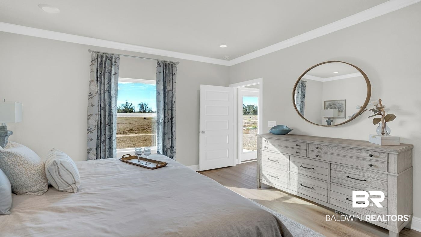 13312 Shea Circle Foley, AL 36535 - Photo 15 of 17 Bedroom featuring wood-finish flooring, a double window with patterned drapes, a white paneled door providing outdoor access, and crown molding