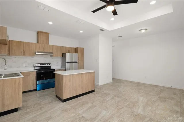 a kitchen with kitchen island stainless steel appliances a stove refrigerator sink and cabinets