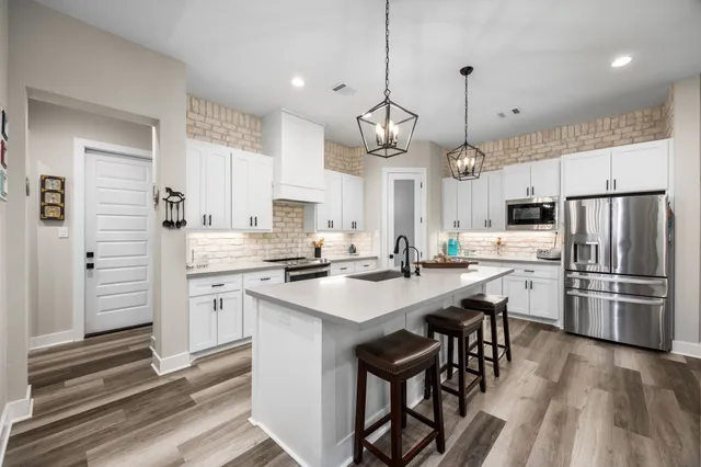 a kitchen with stainless steel appliances a stove a sink a refrigerator and white cabinets with wooden floor