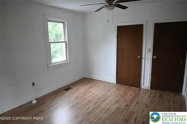an empty room with wooden floor closet and windows
