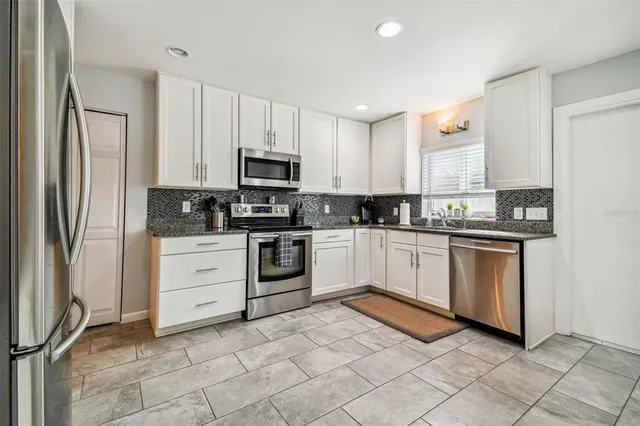 a kitchen with stainless steel appliances granite countertop a refrigerator sink and white cabinets