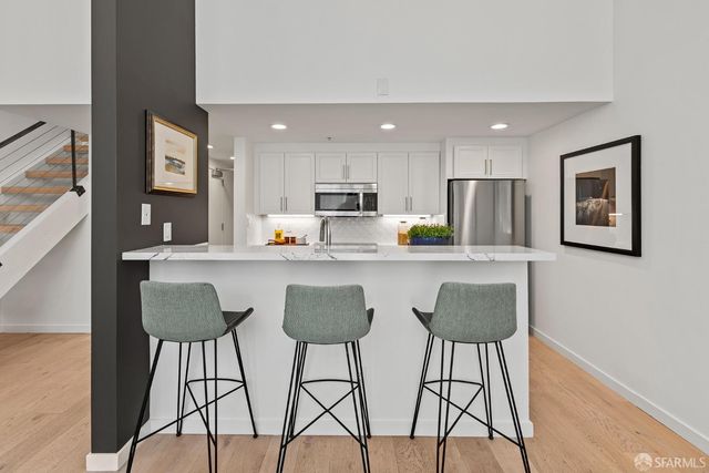 a kitchen with stainless steel appliances granite countertop a refrigerator a sink a stove a dining table and chairs with wooden floor