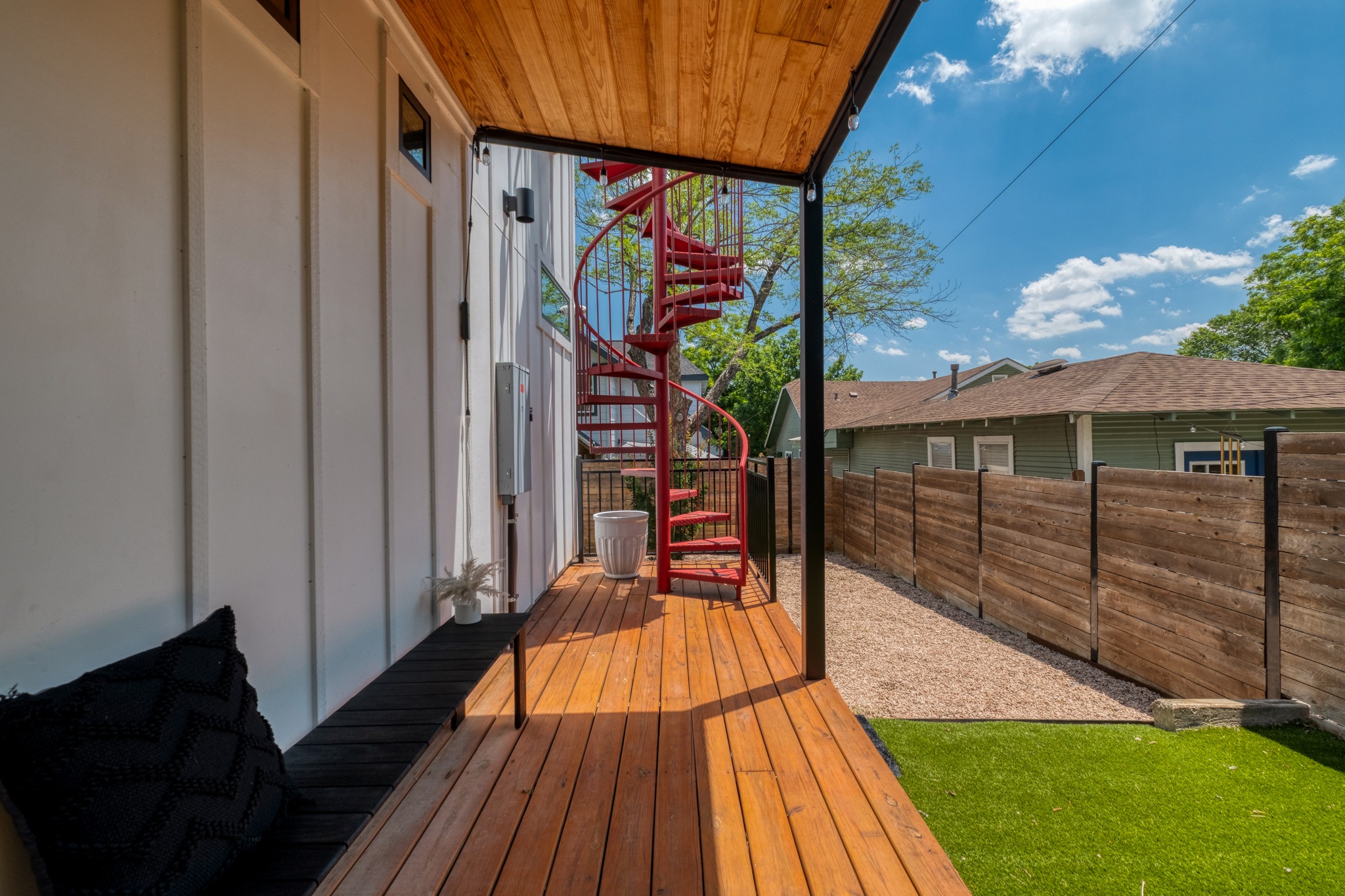 1904 East 16th Street, Unit 2 Austin, TX 78702 - Photo 5 of 20 Expansive outdoor deck featuring wood-finish flooring, a vibrant red spiral staircase, a wood-slat privacy fence, and a section of artificial turf