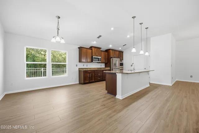 a view of kitchen with kitchen island stainless steel appliances wooden floor cabinets and a window
