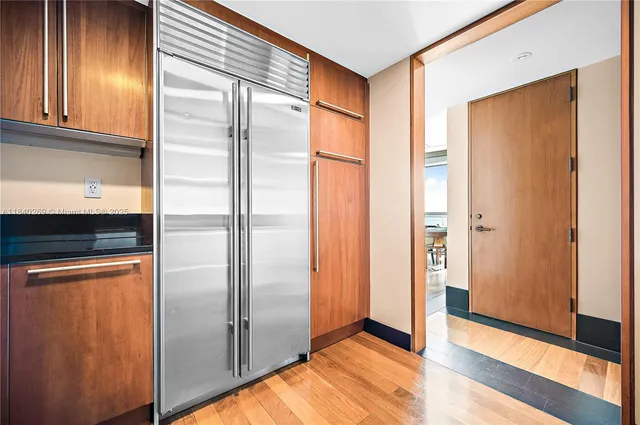 a view of a refrigerator in kitchen and an empty room with wooden floor