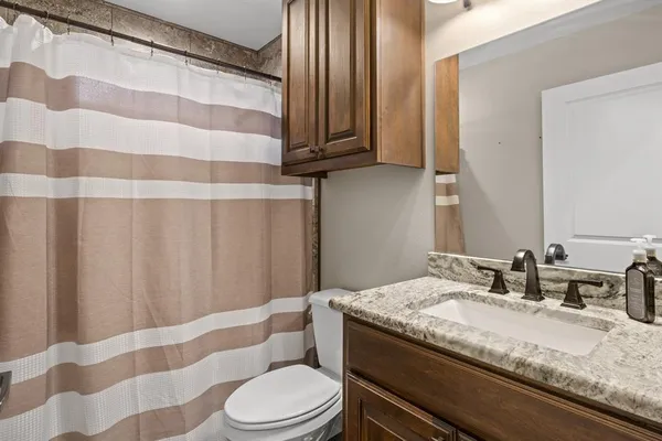 a bathroom with a granite countertop sink toilet a mirror and shower curtain