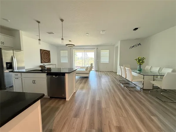 a kitchen with granite countertop a stove a sink a refrigerator and white cabinets with wooden floor